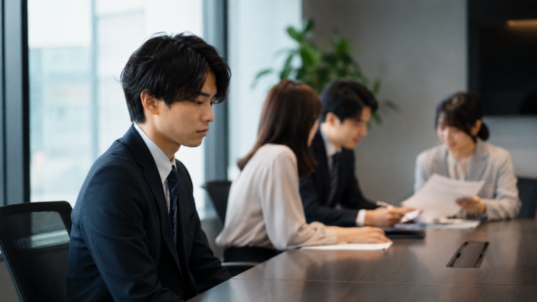 会議から少し離れた席で、不安そうにうつむく若手社員