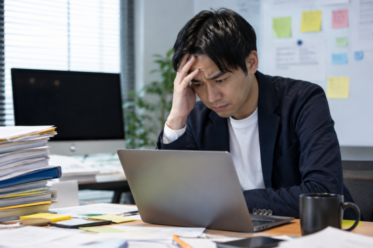段取りが崩れて仕事に追われ、パソコンの前で頭を抱える会社員