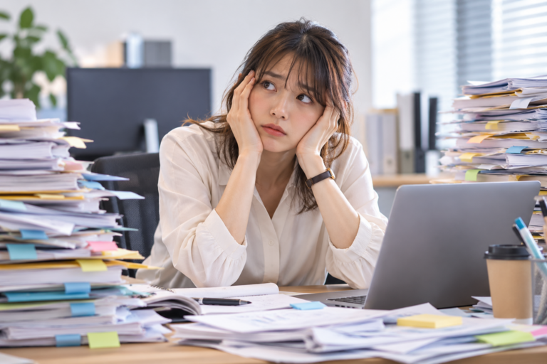 大量の書類に囲まれ、何から仕事を始めるか迷っている会社員